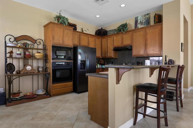 kitchen featuring a breakfast bar, tasteful backsplash, dark stone counters, light tile patterned floors, and black appliances