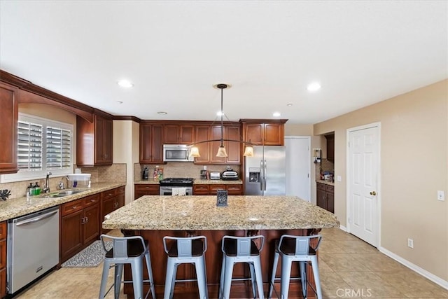 kitchen with pendant lighting, sink, a kitchen island, light stone counters, and stainless steel appliances