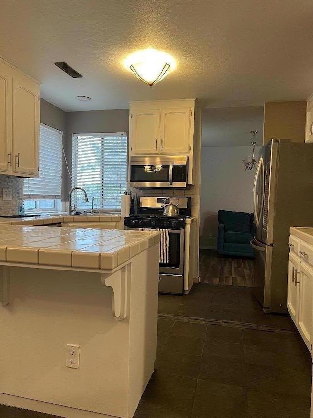 kitchen with backsplash, white cabinetry, tile counters, and stainless steel appliances