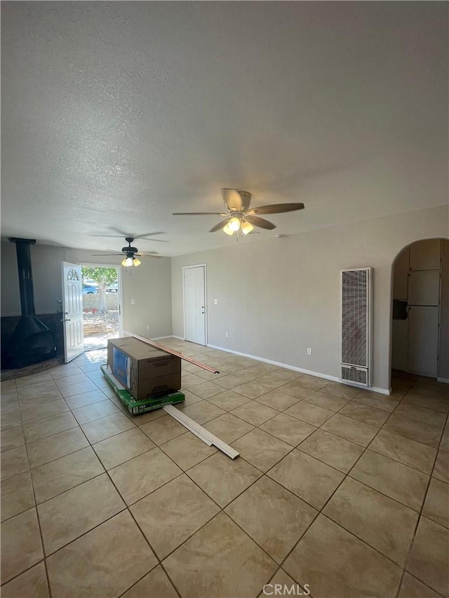 unfurnished living room with a wood stove, ceiling fan, and light tile patterned floors