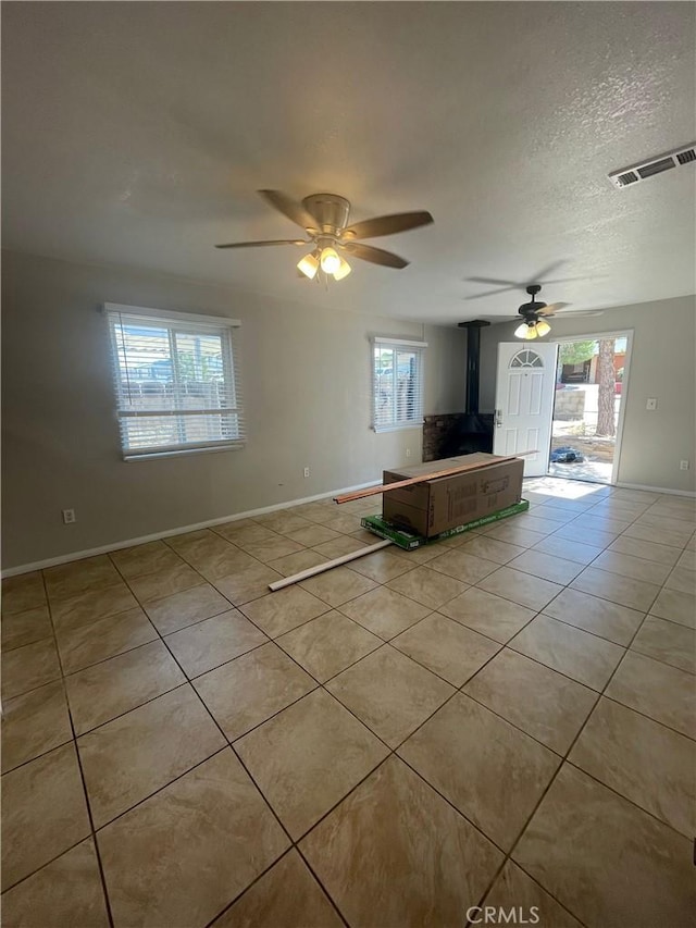 unfurnished living room with light tile patterned floors, a wood stove, ceiling fan, and a healthy amount of sunlight