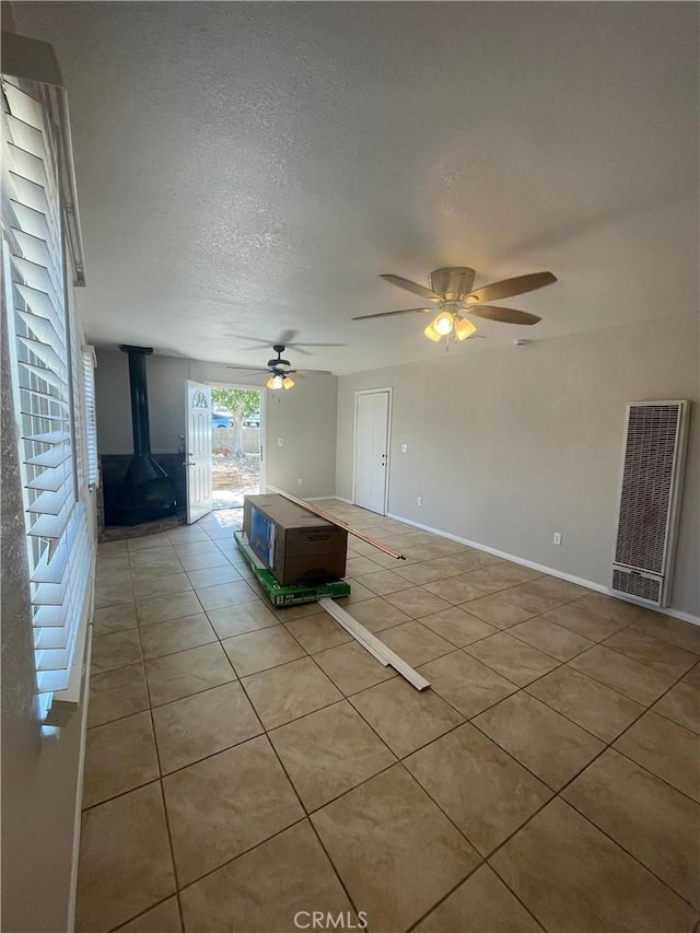 unfurnished living room featuring a textured ceiling, a wood stove, ceiling fan, and light tile patterned flooring