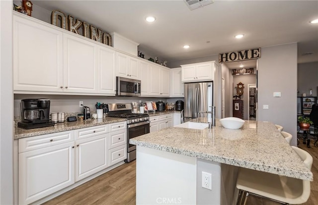 kitchen with white cabinetry, light hardwood / wood-style floors, a kitchen bar, a center island with sink, and appliances with stainless steel finishes