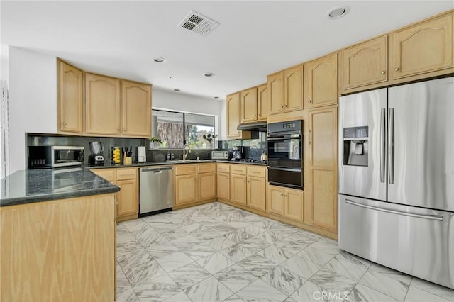 kitchen featuring appliances with stainless steel finishes, light brown cabinetry, tasteful backsplash, sink, and dark stone countertops