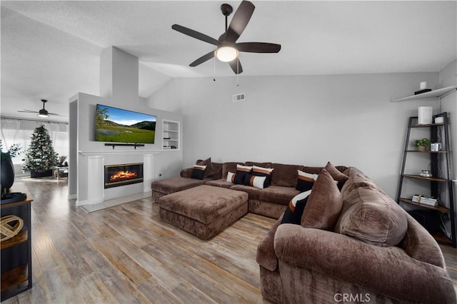 living room with ceiling fan, vaulted ceiling, and light wood-type flooring