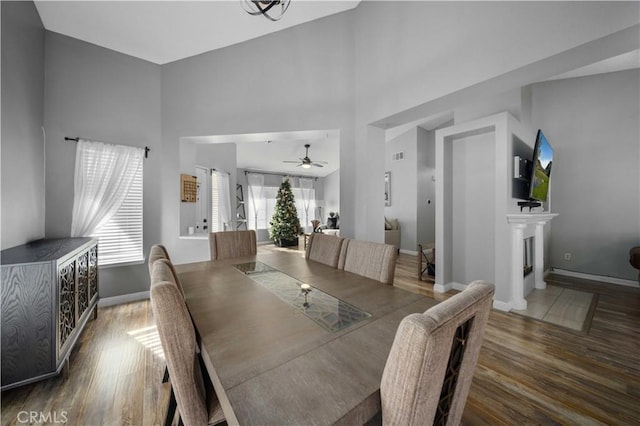 dining space with ceiling fan, a high ceiling, and dark hardwood / wood-style floors