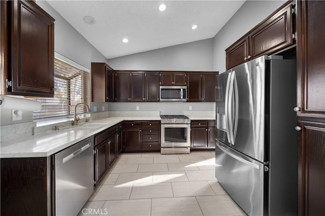 kitchen with dark brown cabinetry, stainless steel appliances, vaulted ceiling, sink, and light tile patterned flooring