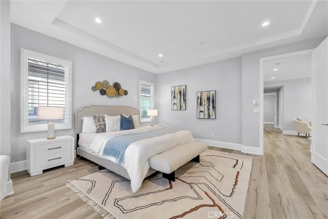 bedroom with light wood-type flooring and a tray ceiling