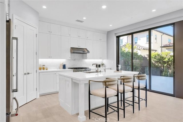 kitchen featuring a center island with sink, sink, white cabinetry, a kitchen breakfast bar, and stainless steel fridge