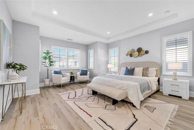 bedroom featuring multiple windows, a tray ceiling, and light hardwood / wood-style flooring