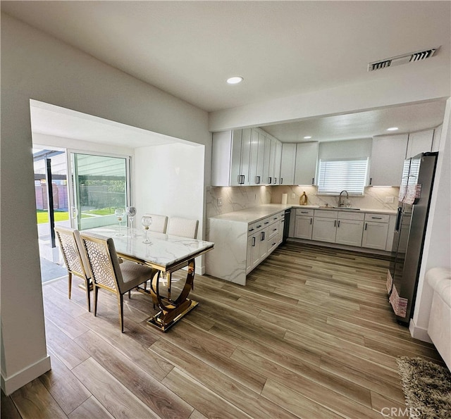 kitchen featuring tasteful backsplash, sink, light hardwood / wood-style flooring, white cabinets, and stainless steel fridge