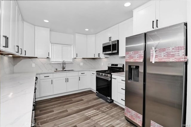 kitchen with stainless steel appliances, dark wood-type flooring, white cabinets, light stone counters, and sink