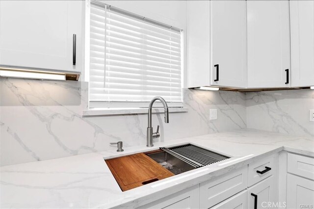 kitchen featuring decorative backsplash, sink, white cabinetry, and light stone counters