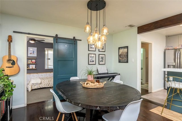 dining room with a barn door, ceiling fan, beamed ceiling, and dark hardwood / wood-style floors