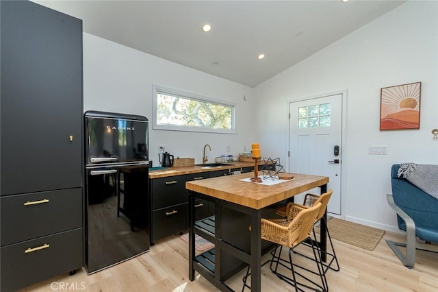 kitchen with light wood-type flooring, lofted ceiling, sink, and black fridge