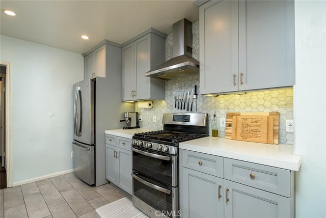 kitchen featuring gray cabinetry, wall chimney range hood, light tile patterned floors, tasteful backsplash, and stainless steel appliances