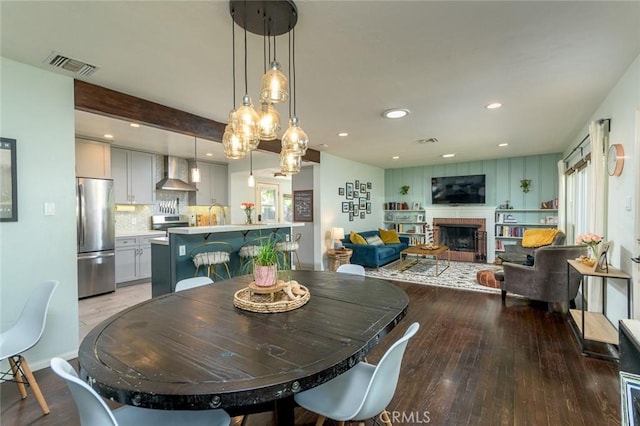 dining space with a fireplace, beamed ceiling, and wood-type flooring