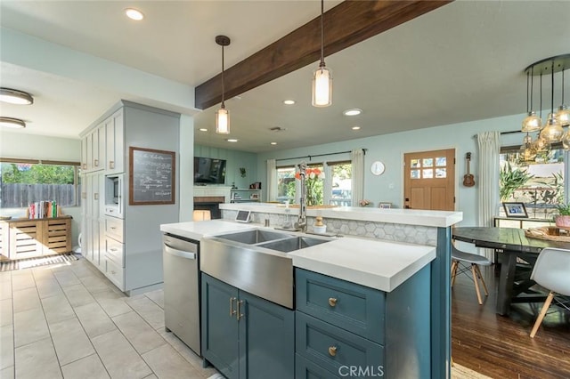 kitchen featuring dishwasher, white cabinets, an island with sink, decorative light fixtures, and beam ceiling