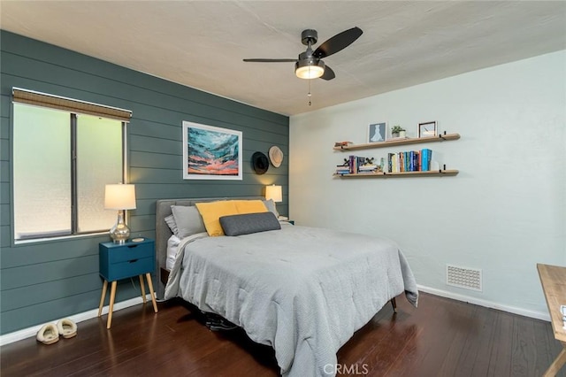 bedroom featuring wood walls, ceiling fan, and dark wood-type flooring