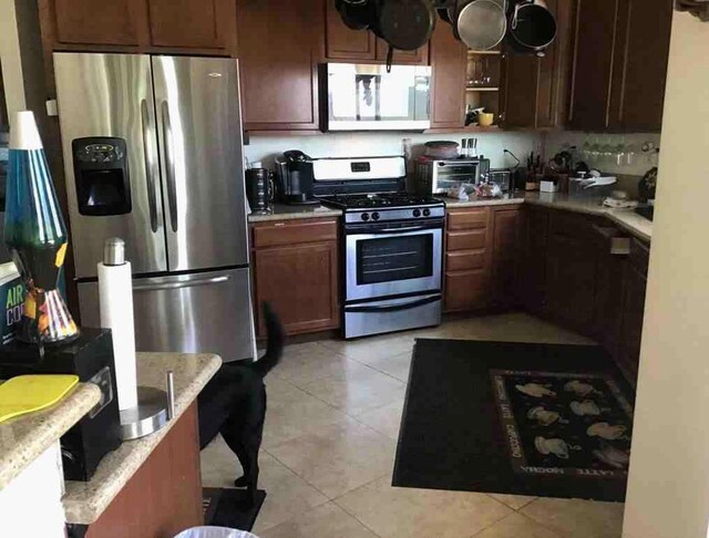 kitchen with light tile patterned floors, stainless steel appliances, and light stone counters