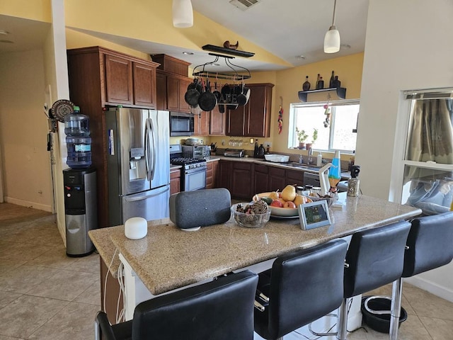 kitchen featuring appliances with stainless steel finishes, lofted ceiling, a kitchen bar, decorative light fixtures, and light tile patterned floors