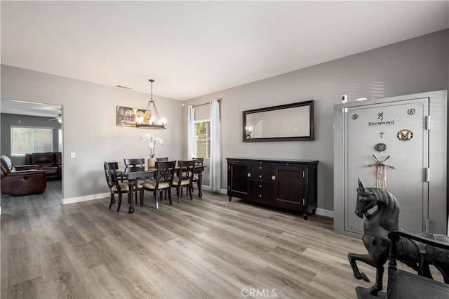 dining area with ceiling fan with notable chandelier, light wood-type flooring, and a wealth of natural light