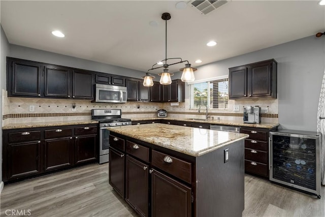 kitchen featuring appliances with stainless steel finishes, beverage cooler, sink, a center island, and hanging light fixtures