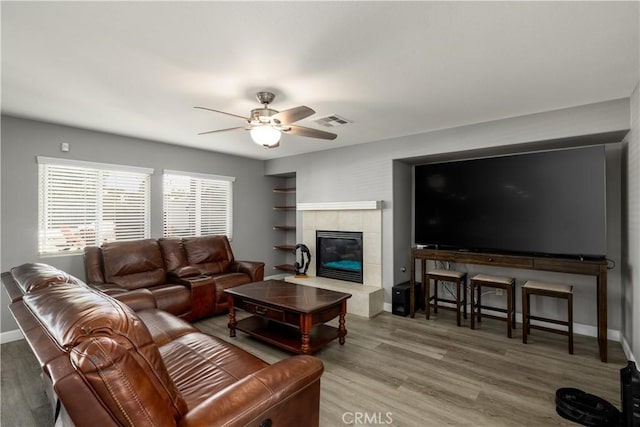 living room with a tiled fireplace, ceiling fan, and wood-type flooring