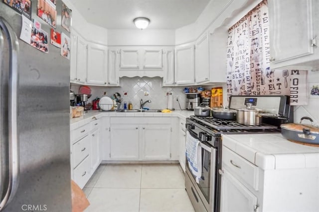 kitchen featuring tile countertops, sink, white cabinetry, appliances with stainless steel finishes, and light tile patterned floors