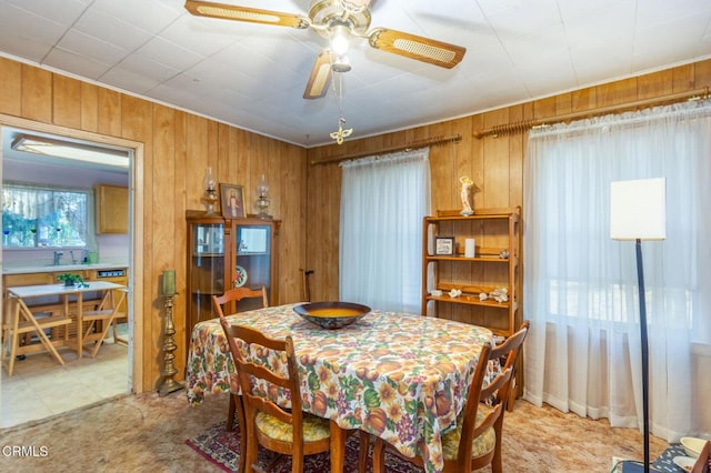 carpeted dining room with ceiling fan, sink, and wooden walls