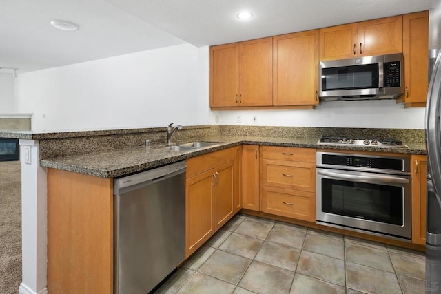 kitchen with dark stone countertops, kitchen peninsula, sink, and appliances with stainless steel finishes