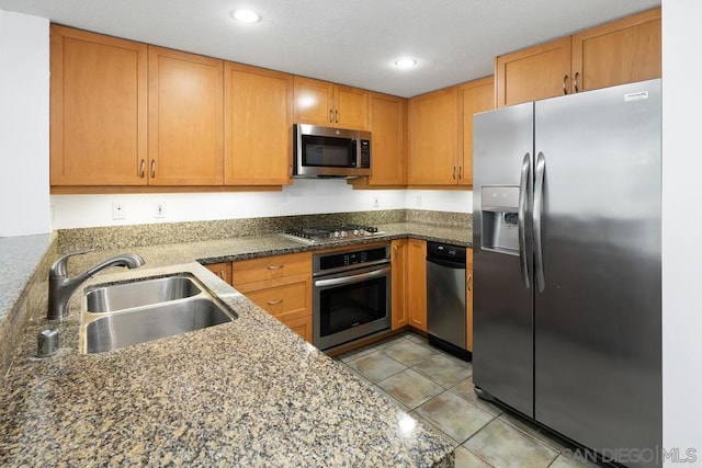 kitchen featuring light tile patterned floors, stainless steel appliances, dark stone countertops, and sink