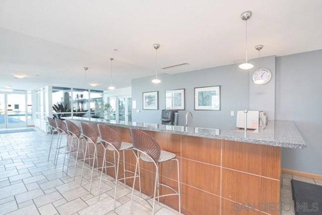 kitchen featuring a kitchen breakfast bar, kitchen peninsula, light stone counters, and hanging light fixtures