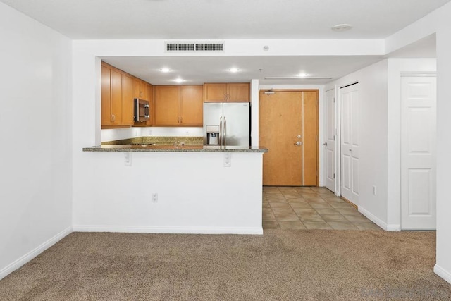 kitchen featuring stainless steel appliances, a kitchen breakfast bar, kitchen peninsula, dark stone countertops, and light colored carpet