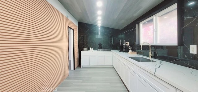 kitchen featuring sink, light wood-type flooring, tasteful backsplash, light stone counters, and white cabinetry