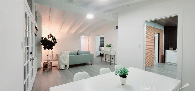 dining area with lofted ceiling with beams, french doors, and light hardwood / wood-style flooring