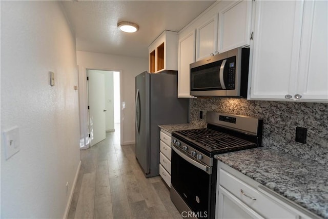 kitchen featuring light stone countertops, white cabinetry, light hardwood / wood-style flooring, and stainless steel appliances