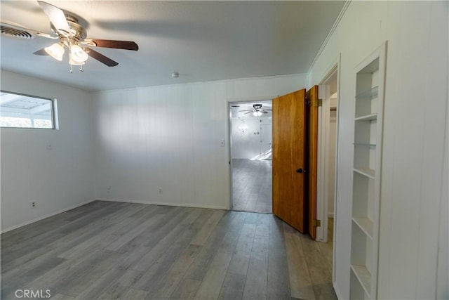 unfurnished room with built in shelves, light wood-type flooring, and crown molding