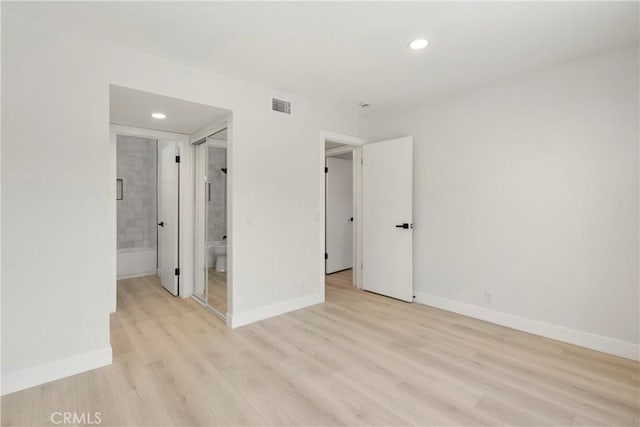 unfurnished bedroom featuring ensuite bathroom and light hardwood / wood-style floors