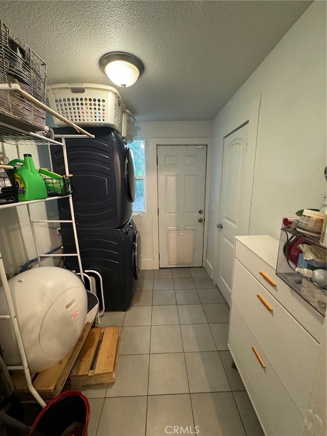 clothes washing area featuring a textured ceiling, laundry area, tile patterned flooring, and stacked washer and clothes dryer