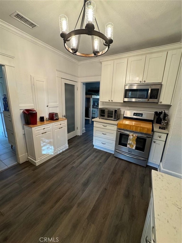 kitchen featuring visible vents, ornamental molding, white cabinetry, a chandelier, and appliances with stainless steel finishes