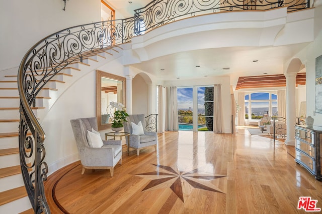 foyer featuring a towering ceiling, light hardwood / wood-style floors, and ornate columns