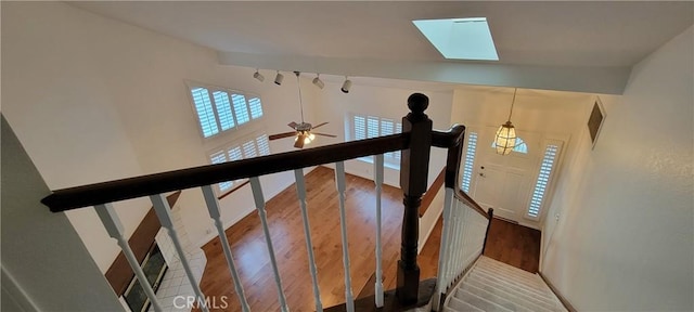 staircase featuring ceiling fan, rail lighting, hardwood / wood-style flooring, and lofted ceiling with skylight