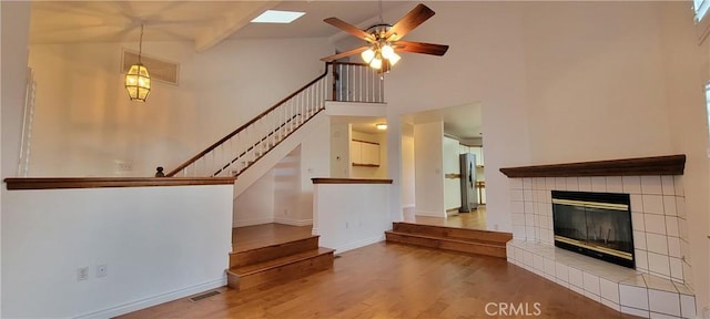 unfurnished living room with ceiling fan, a tile fireplace, beam ceiling, hardwood / wood-style flooring, and high vaulted ceiling