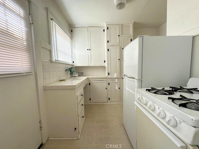 kitchen with tile countertops, tasteful backsplash, white cabinetry, and gas range gas stove