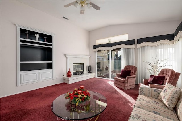 carpeted living room with ceiling fan, built in shelves, vaulted ceiling, and a healthy amount of sunlight