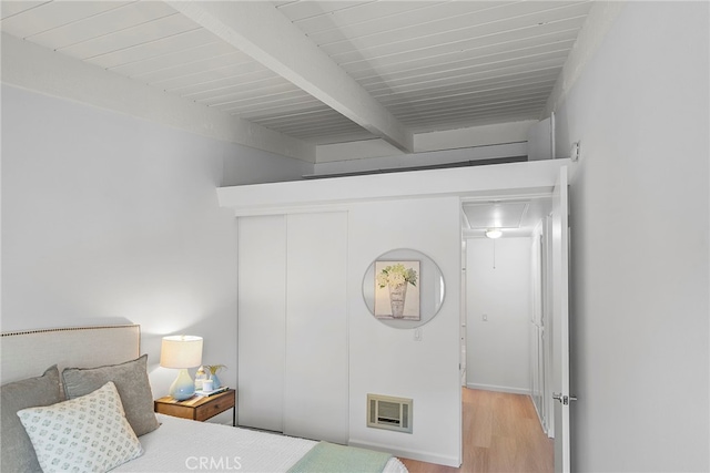 bedroom featuring light hardwood / wood-style floors, beam ceiling, and a closet