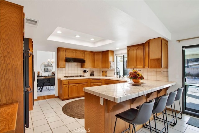 kitchen with a tray ceiling, tile countertops, kitchen peninsula, and light tile patterned floors