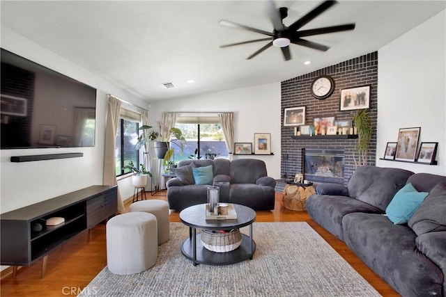 living room with hardwood / wood-style flooring, a brick fireplace, ceiling fan, and lofted ceiling