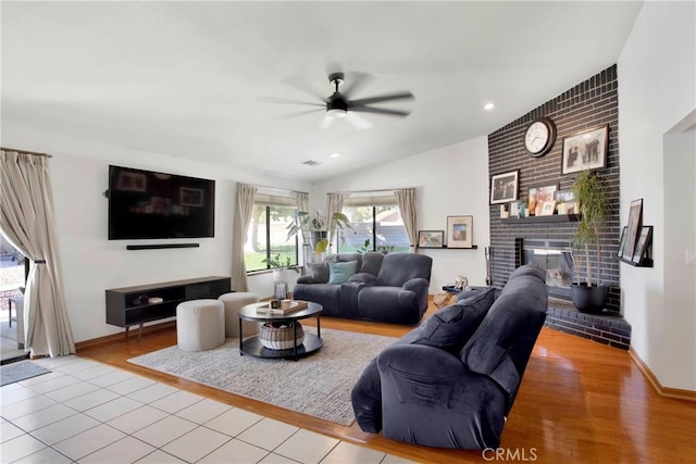 living room featuring a fireplace, light hardwood / wood-style floors, vaulted ceiling, and ceiling fan